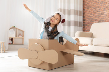 Cute little girl playing with cardboard airplane in living room