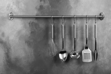 Rack with clean kitchen utensils on grey wall. Space for text