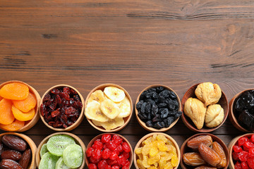 Bowls of different dried fruits on wooden background, top view with space for text. Healthy lifestyle
