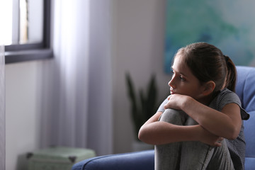 Depressed preteen girl sitting in armchair at home