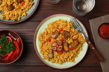 Flat lay composition with plate of rice pilaf and meat on wooden background