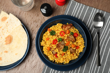 Flat lay composition with plate of rice pilaf and meat on wooden background