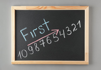 Obraz premium Chalkboard with word FIRST and numbers on grey background, top view. Victory concept