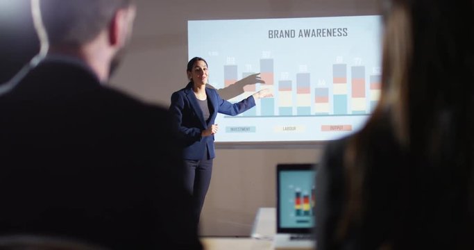 4K Marketing businesswoman giving a presentation, showing animated graphs on screen. Slow motion.