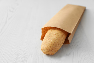 Baguette in paper bag on wooden table. Space for text