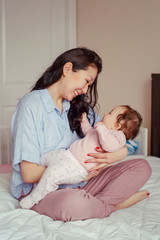 Portrait of beautiful smiling laughing mixed race Asian mother playing with her cute adorable newborn infant baby. Early development and health care lifestyle concept. Family in bedroom