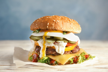 Tasty burger with fried egg on parchment against color background