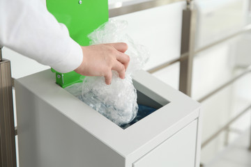 Young woman throwing plastic film in metal bin indoors, closeup. Waste recycling