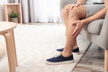 Man suffering from leg pain at home, closeup. Space for text