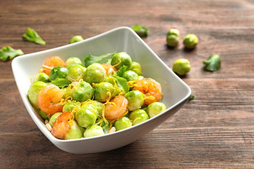 Bowl of delicious salad with Brussels sprouts and shrimps on wooden table