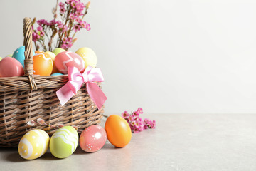 Wicker basket with painted Easter eggs and flowers on table, space for text