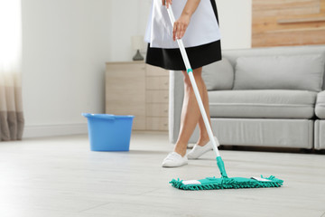 Young maid washing floor with mop in hotel room, closeup