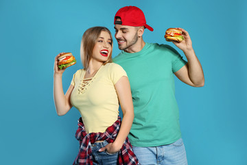 Happy couple with tasty burgers on color background