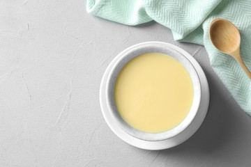 Bowl of condensed milk served on grey table, top view with space for text. Dairy products