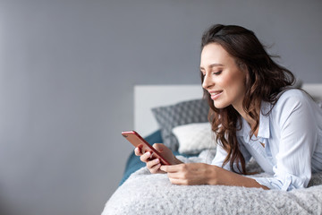 Woman using cellphone bed at home.