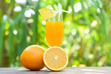 Orange juice with piece orange fruit on glass with nature green summer background
