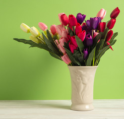 Colorful tulips in vase on white table wall green background
