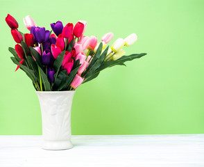 Colorful tulips in vase on white table wall green background