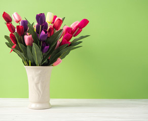 Colorful tulips in vase on white table wall green background