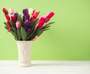 Colorful tulips in vase on white table wall green background