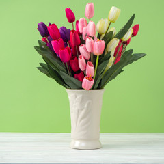 Colorful tulips in vase on white table wall green background