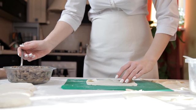 Girl in an apron preparing envelopes with mushrooms for baking at home.