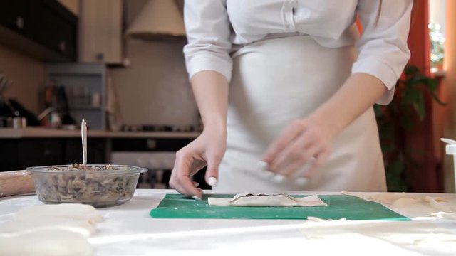 Girl in an apron preparing envelopes with mushrooms for baking at home.