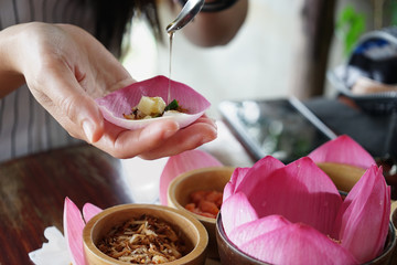 Young woman is pouring sweet sauce into the side dish that is wrapped in a lotus leaf called Miang kham to eat.