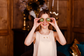 a young woman shows two halves of kiwi indoors. close his eyes. Fruit diet