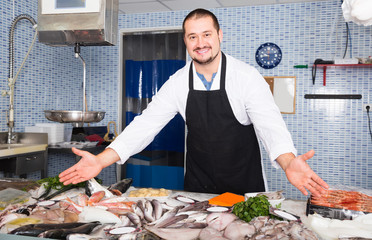 cheerful man in black apron standing near fish counter