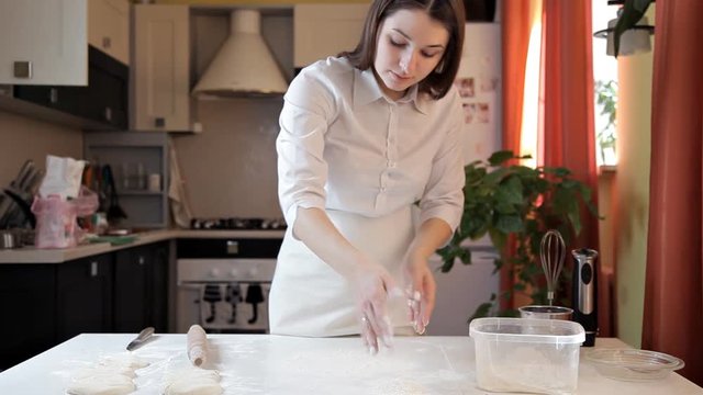 The girl in the apron rolls out the pizza dough with a rolling pin. Cooking pizza at home