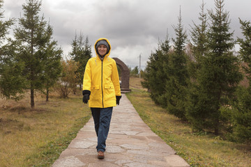 young woman in raincoat walks in park in cloudy weather, copy space