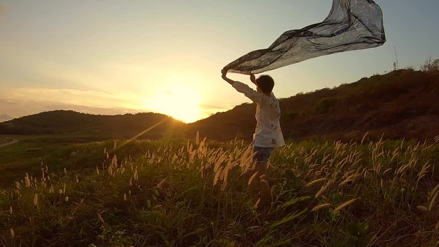 video footage , woman stands with fabric in hands on grass field at evening time .