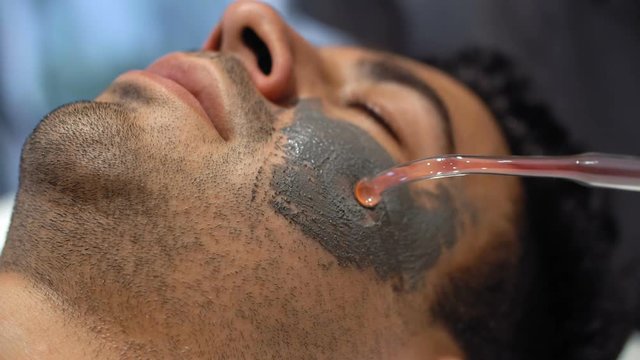 Close up of male face and special tool applying organic scrub on it