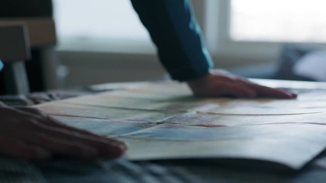 Close-up of hiker putting down and straighten a big map on the table.