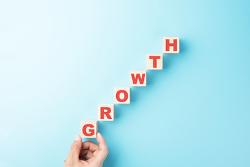 Hand holding wooden cube with text growth isolated on blue background growing businees concept