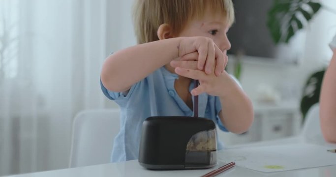 Boy sharpening a colored pencil in a sharpener sitting at the kitchen table