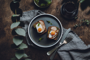 Ham and Fried Quail Egg Toast with Mustard and Basil on a dark wooden background, top view