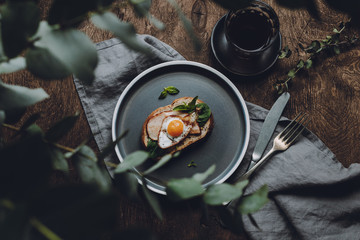 Ham and Fried Quail Egg Toast with Mustard and Basil on a dark wooden background, top view