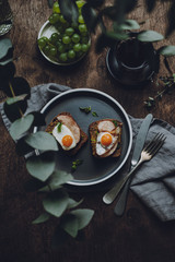 Ham and Fried Quail Egg Toast with Mustard and Basil on a dark wooden background, top view