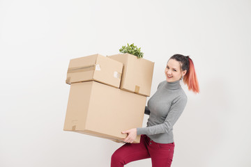 A young woman carries heavy cardboard boxes with things. White light apartment.