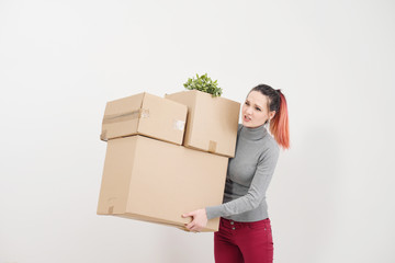 A young woman carries heavy cardboard boxes with things. White light apartment.