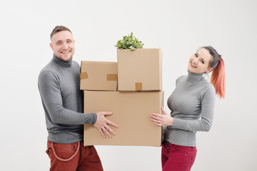 A young woman and a man carry heavy cardboard boxes with things. White light apartment. They laugh and kiss.
