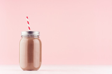 Sweet chocolate milkshake in old fashioned jars with  straw, silver cap on light pastel pink background.