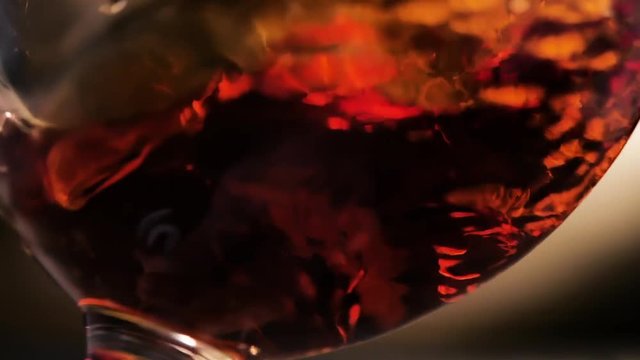 Cognac is rotated in a glass. On dark background.