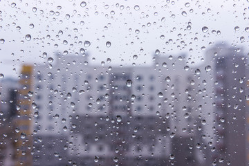 View through glass window of high-rise building on a rainy. Rain drops on window. blurred high-rise building on glass