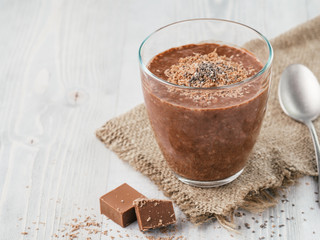 Chocolate chia pudding in glass and chocolate cubes slice with rustic napkin on gray wooden table....