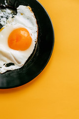 Copy space breakfast with scrambled eggs in black plate on yellow background