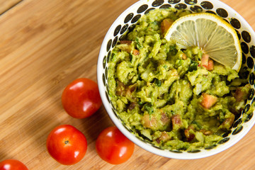 Bowl of guacamole with limon and tomato on wood texture table