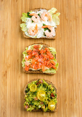 Open sandviches with guacamole, salmon and prawn on wood texture  background